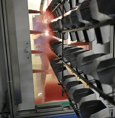 Mitarbeiter beim manuellen Pulverauftrag in der Beschichtungskabine, Bauteile hängen am Gestell