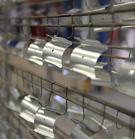 Aluminiumbauteile hängen vor der Pulverbeschichtung an Haken am Warengestell